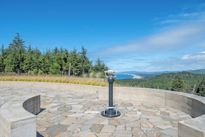 A stone-paved viewing platform with a telescope, overlooking a forested area and a distant coastline. - Seascape North View Townhome, Fireplace & Pet friendly (Depoe Bay)