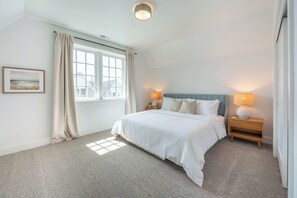 A bedroom with a bed, two bedside lamps, a window with curtains, and a framed picture on the wall. - Seascape North View Townhome, Fireplace & Pet friendly (Depoe Bay)