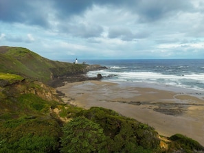 A coastal landscape with a lighthouse, sandy beach, and green hills. - Seascape North View Townhome, Fireplace & Pet friendly (Depoe Bay)