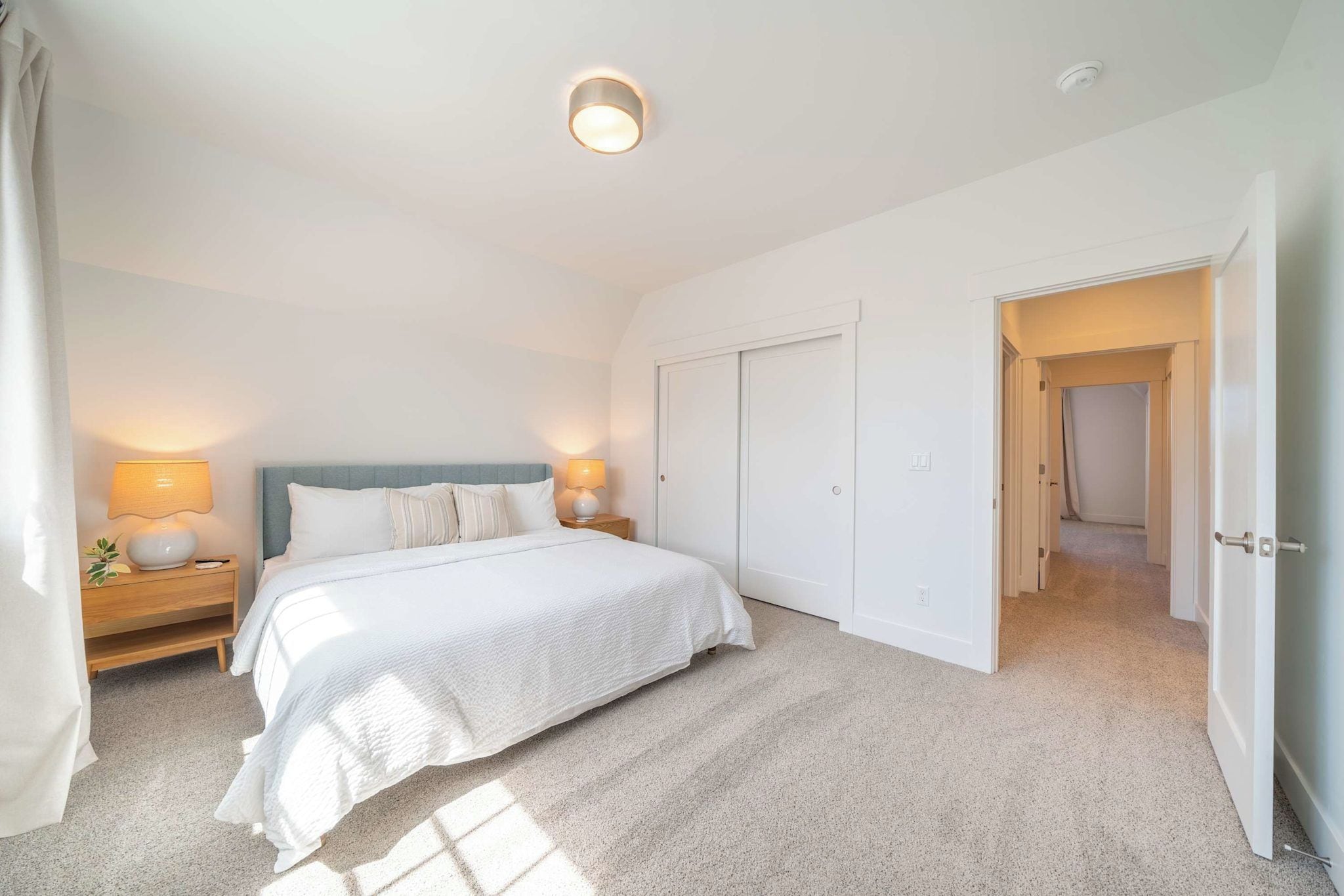 A bedroom with a bed, nightstands, a wardrobe, and a door leading to another room.