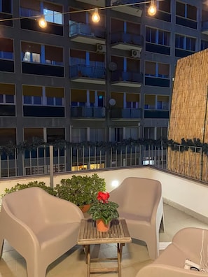 A balcony with two chairs and a small table, overlooking a building with multiple balconies.