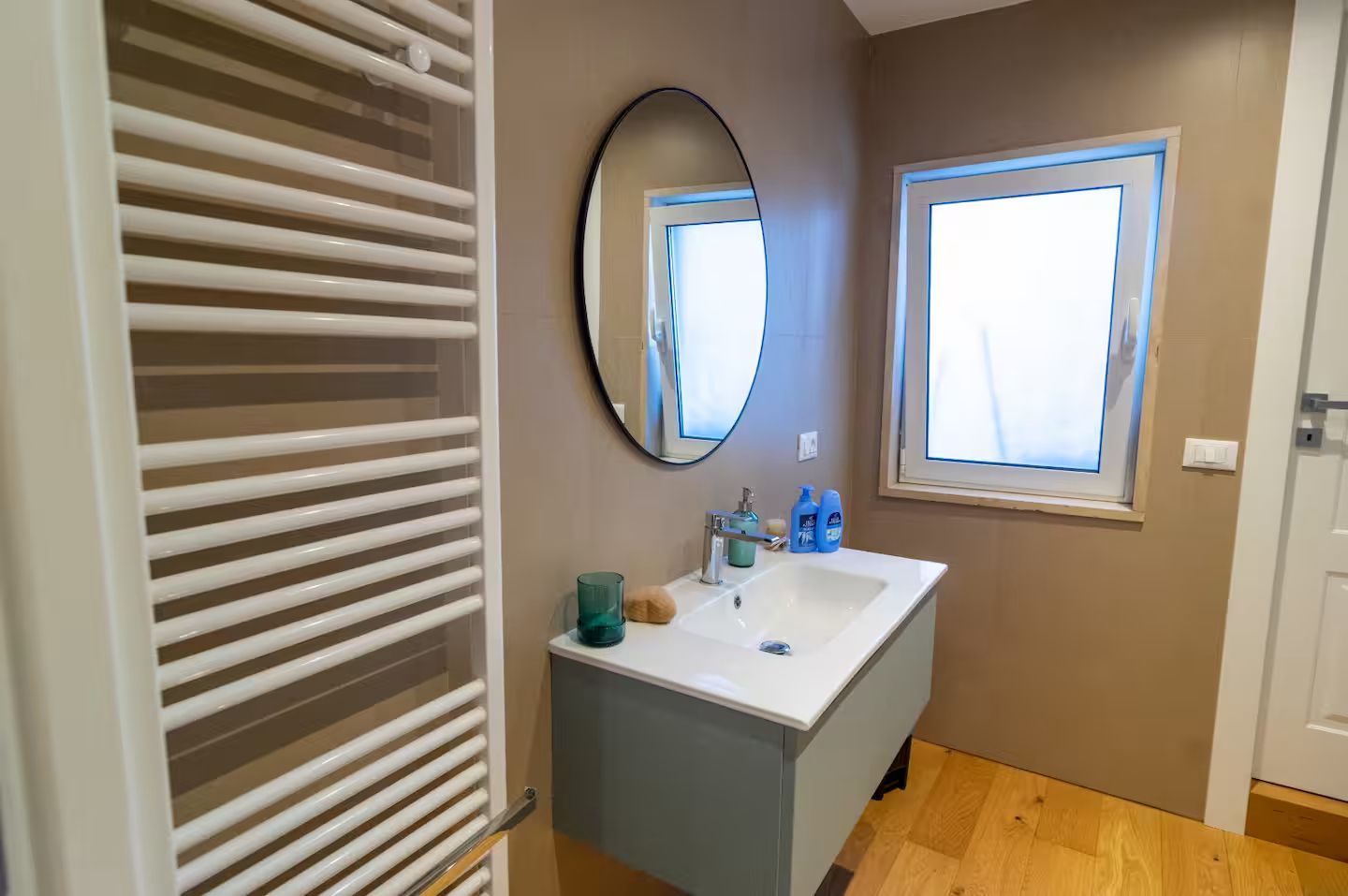 A bathroom with a white vanity, a mirror, a window, and a towel rack.