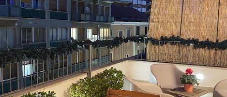 Une terrasse sur le toit, aménagée avec un espace salon, des plantes en pot et des guirlandes lumineuses.