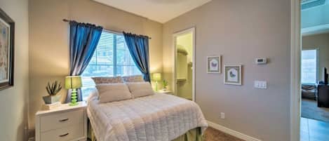 A bedroom with a bed, nightstands, a window with curtains, a mirror, and wall-mounted artwork.