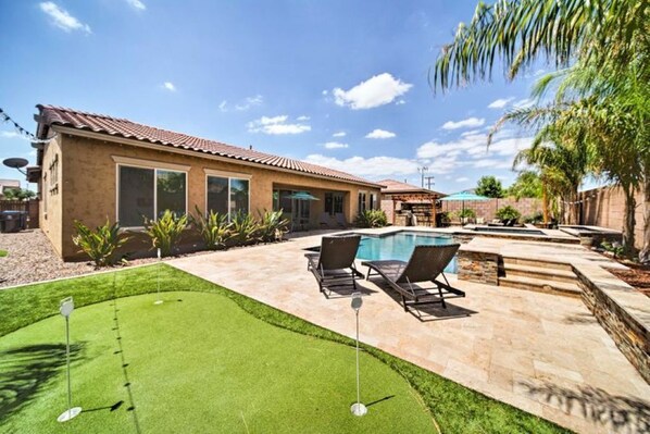 Ein Haus mit Swimmingpool, einer Terrasse mit Liegestühlen und einem gepflegten Rasen.