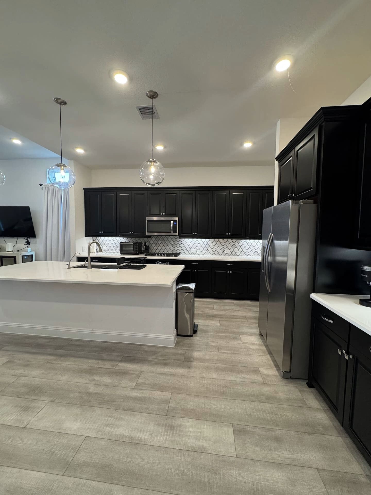 A modern kitchen with dark cabinets, a stainless steel refrigerator, and a central island with a sink.