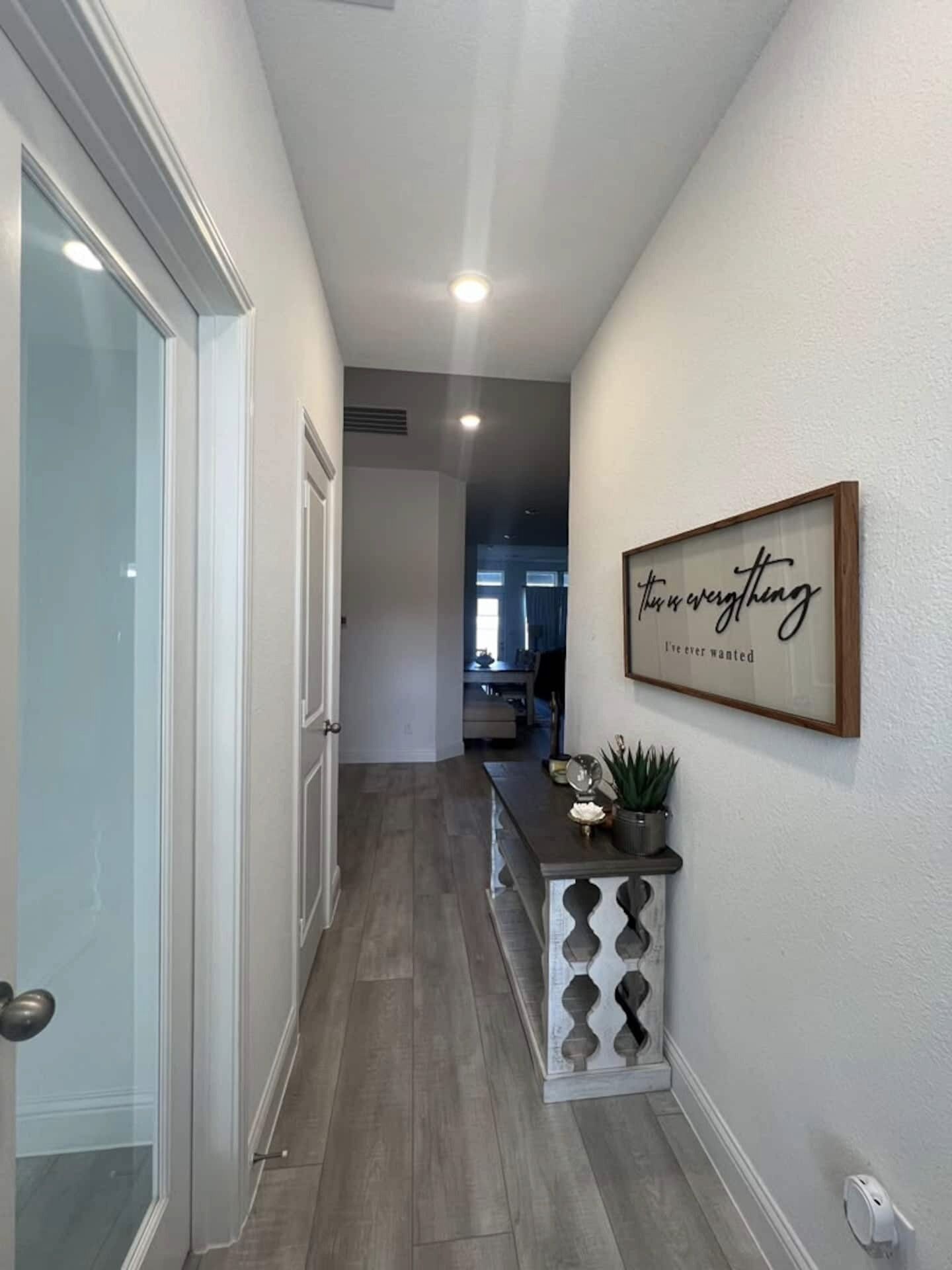 A hallway with a wooden console table, a framed inspirational quote, and a door leading to another room.