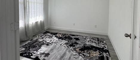 Una habitación con alfombra estampada, una ventana con cortinas y una puerta.