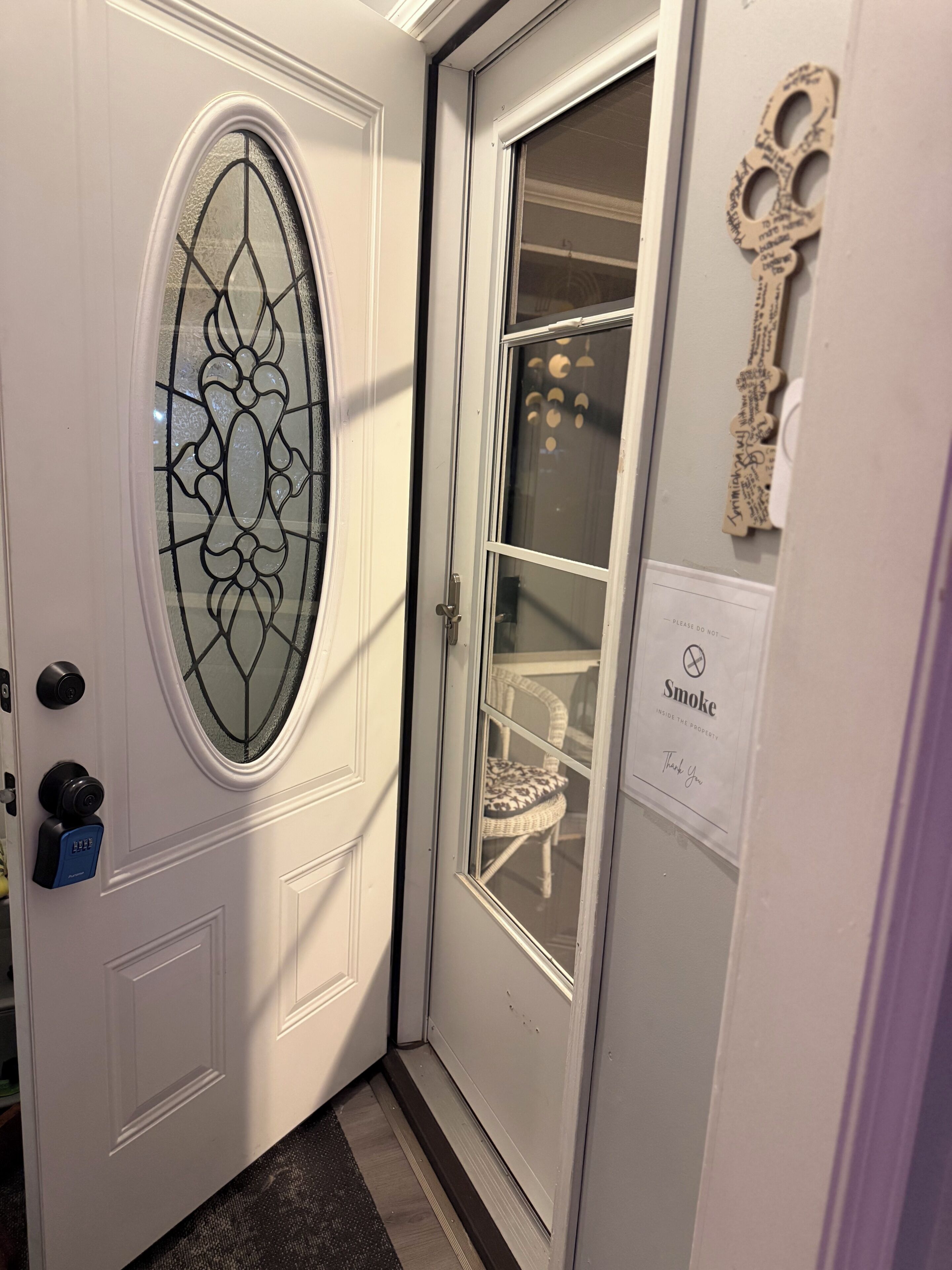 A white door with a glass panel, a key holder, and a 'Smoke Inside the Property' sign.