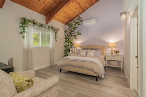 A bedroom with a bed, bedside tables, a nightstand, a window with curtains, a wooden ceiling, and a wall-mounted air conditioner. - The Best Lake View!! (Crestline)