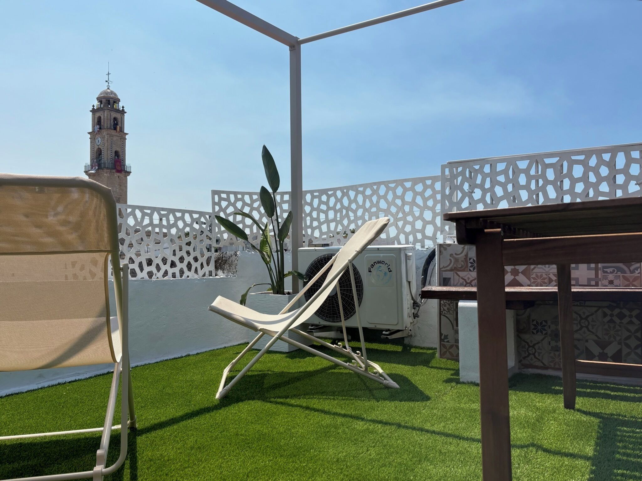 Terraza en la azotea con césped artificial, un ventilador blanco, una silla de lounge y una valla decorativa blanca.