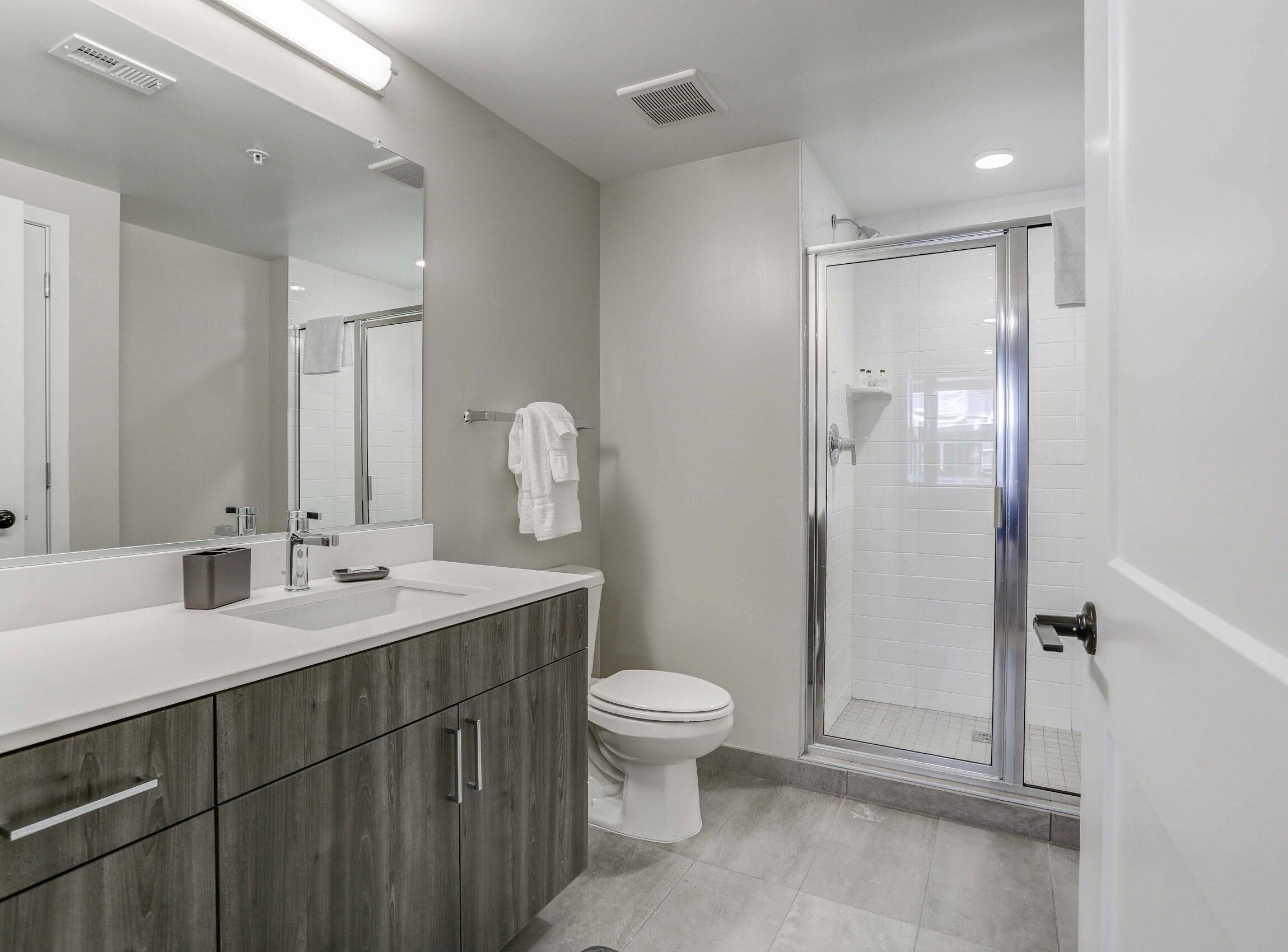 A modern bathroom with a large mirror, a shower enclosure, and a toilet.