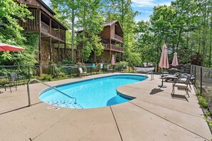Ein Swimmingpool mit Liegestühlen und Sonnenschirmen, umgeben von einer Holzhütte und üppigem Grün.