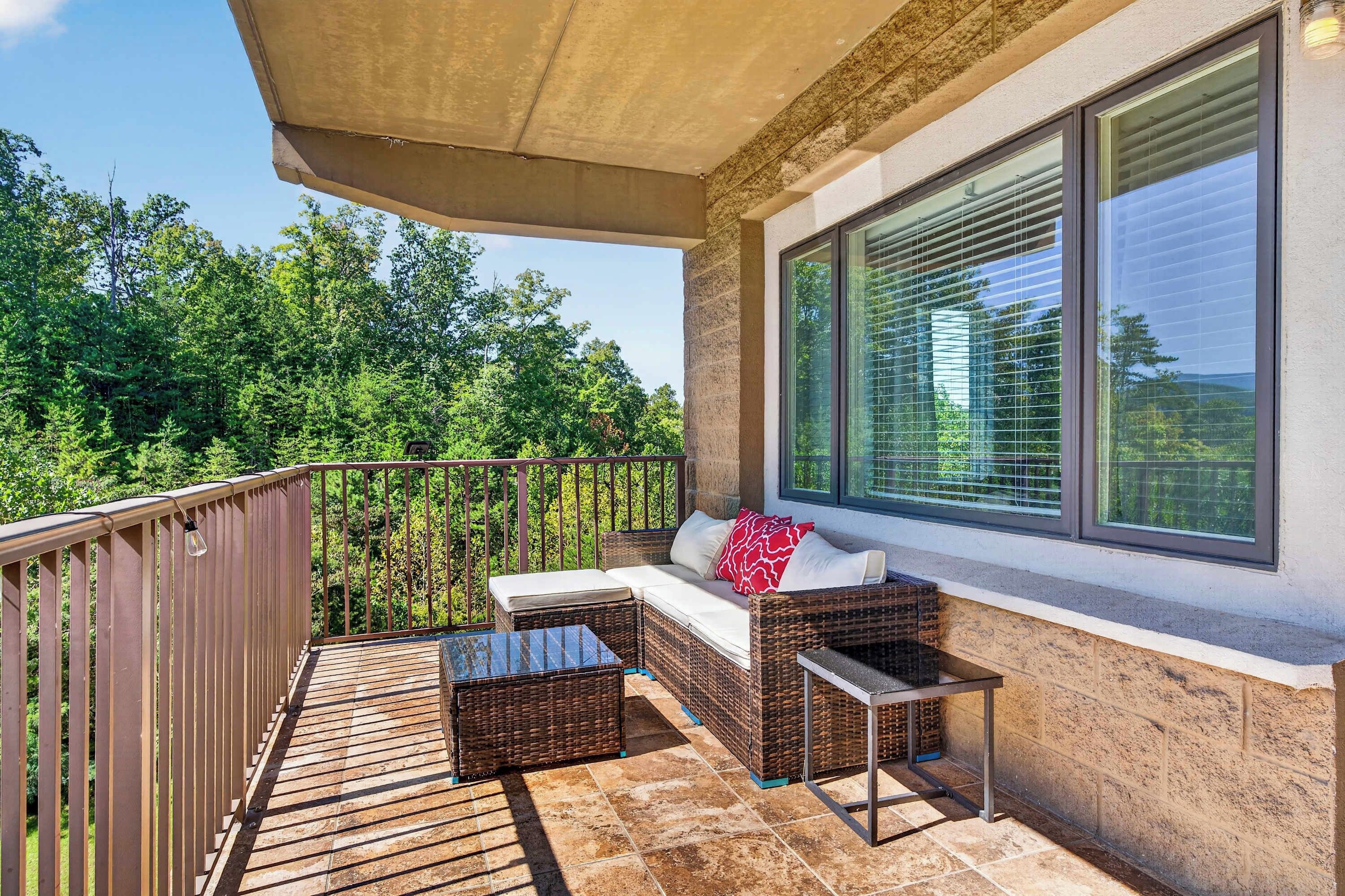 A balcony with a wicker sofa, a small table, and a view of trees.
