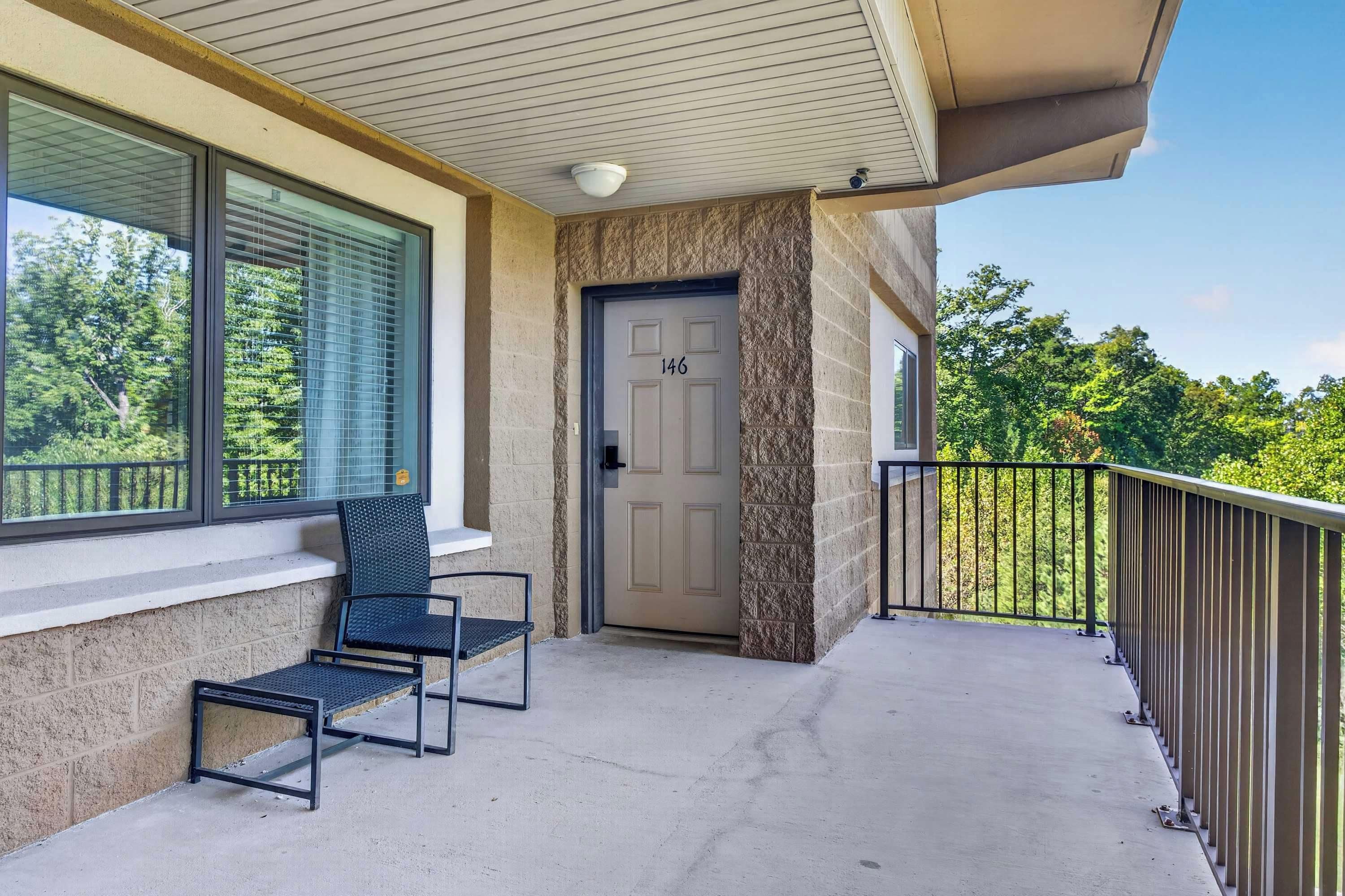 A balcony with two chairs, a door with the number 146, and a view of trees.