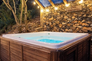 A hot tub in a wooden cabin with a stone wall and a sign that reads 'ZONA COMPARTIDA'.