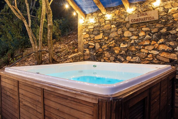 Un jacuzzi en una cabaña de madera con un muro de piedra y un letrero que dice 'ZONA COMPARTIDA'.