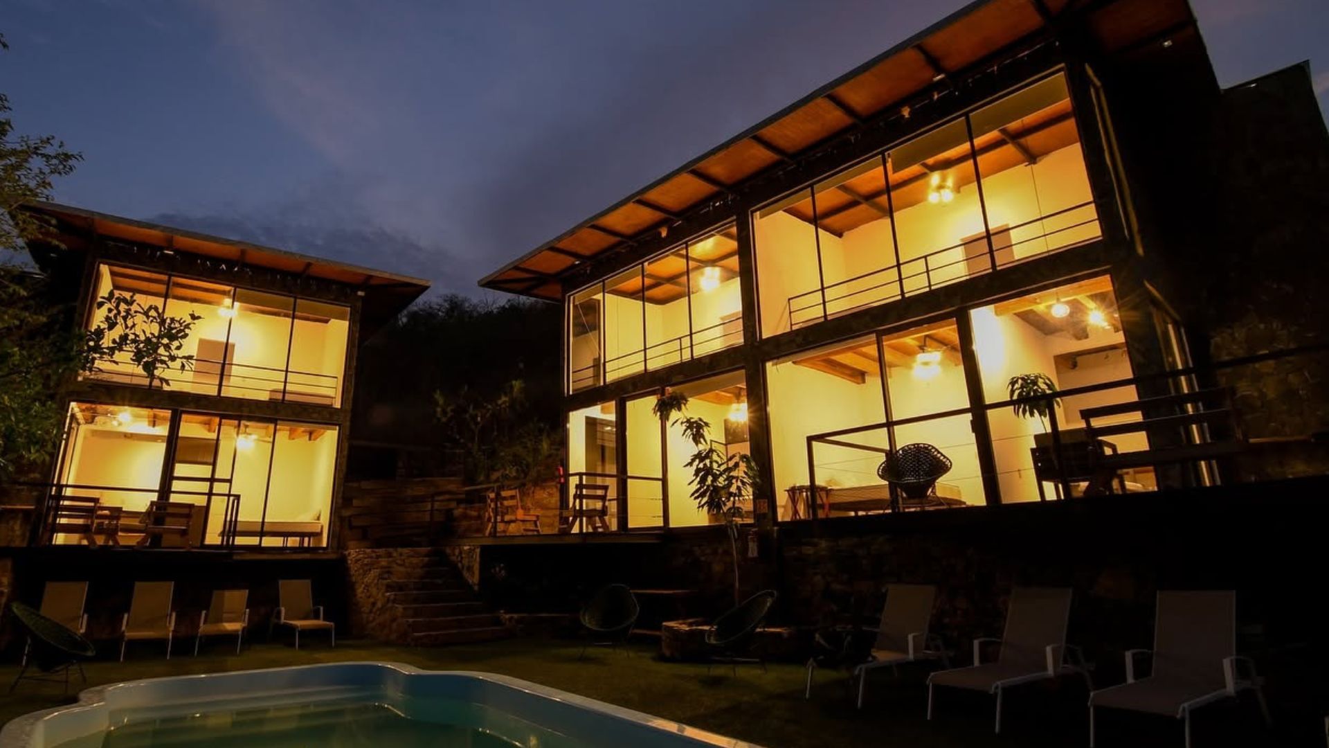 Una moderna casa a due piani con ampie finestre, una piscina e un'area salotto esterna.