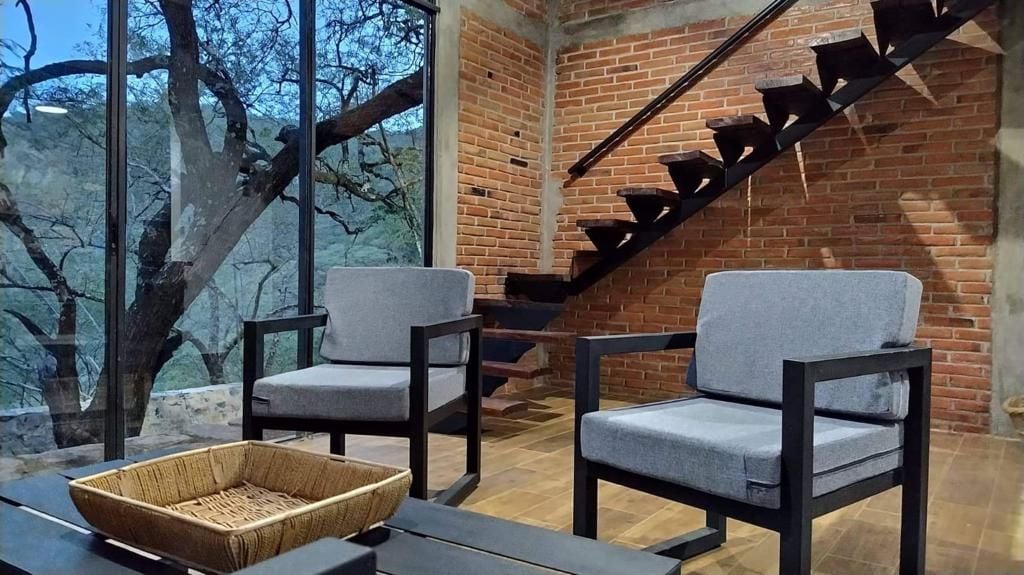 A room with two grey chairs, a woven basket on a table, and a brick wall with a staircase.
