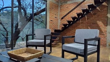 A room with two grey chairs, a woven basket on a table, and a brick wall with a staircase.