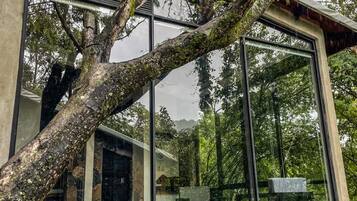 Un edificio moderno con amplios ventanales de vidrio, base de piedra y terraza de madera con mobiliario exterior.