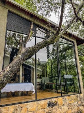A modern building with large glass windows, a stone foundation, and a wooden deck with outdoor furniture.