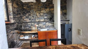 Una cocina compacta con pared de piedra, armarios de madera y un refrigerador negro.