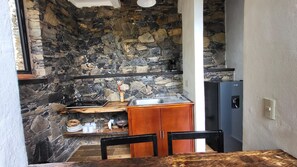 A compact kitchen with a stone wall, wooden cabinets, and a black refrigerator.