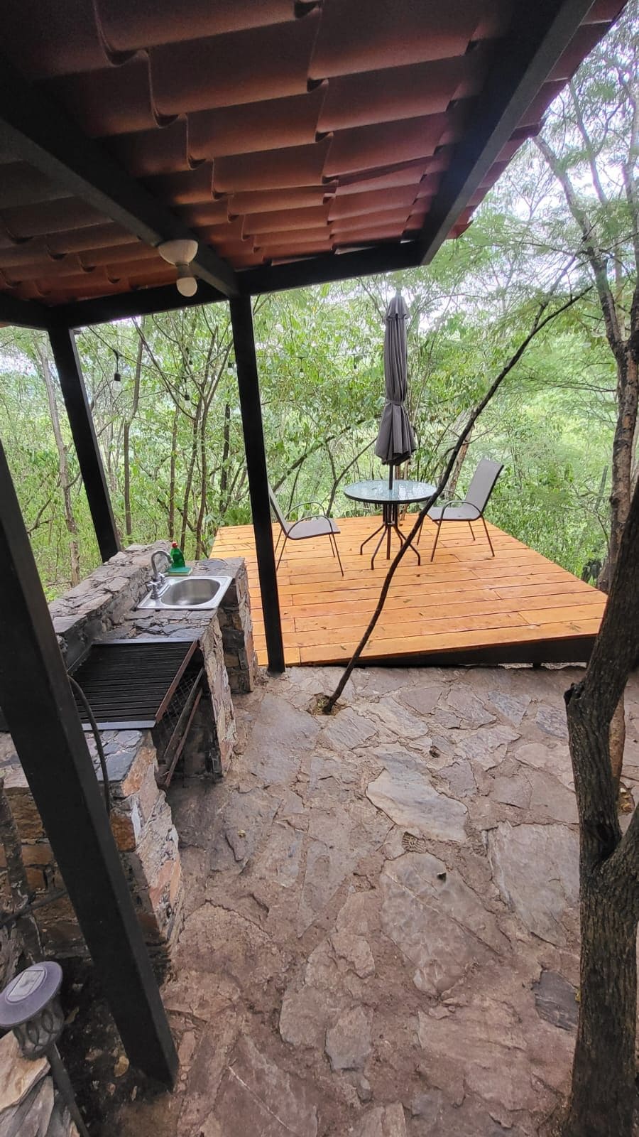 Eine Terrasse im Freien mit Steinboden, einem Tisch, Stühlen und einem Grill.