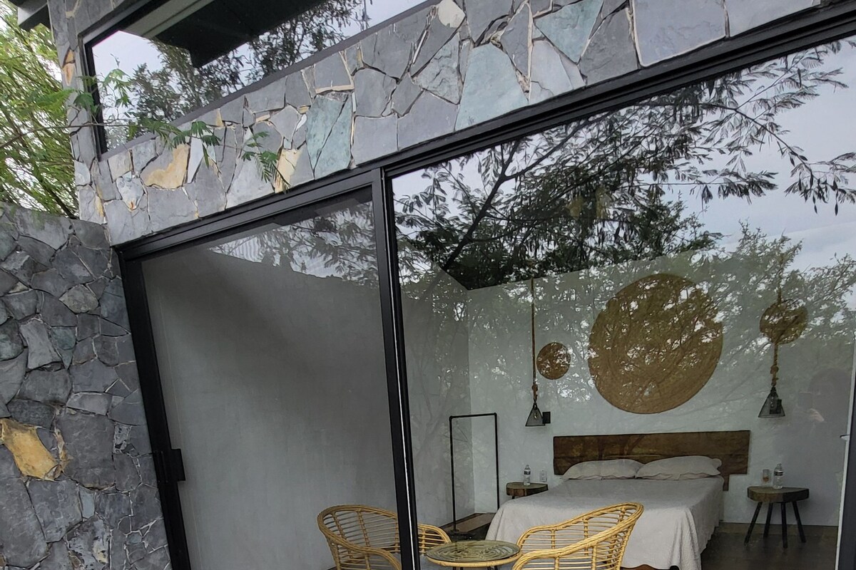 Un baño moderno con pared de piedra, una bañera grande y una zona de ducha con mampara de vidrio y sillones de mimbre.