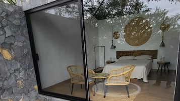 Un baño moderno con pared de piedra, una bañera grande y una zona de ducha con mampara de vidrio y sillones de mimbre.