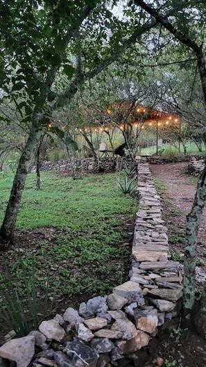 A stone pathway leading through a garden with trees and a stone wall.