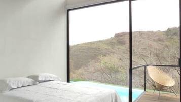 A bedroom with a bed, a ceiling fan, a large window, and a view of a landscape.