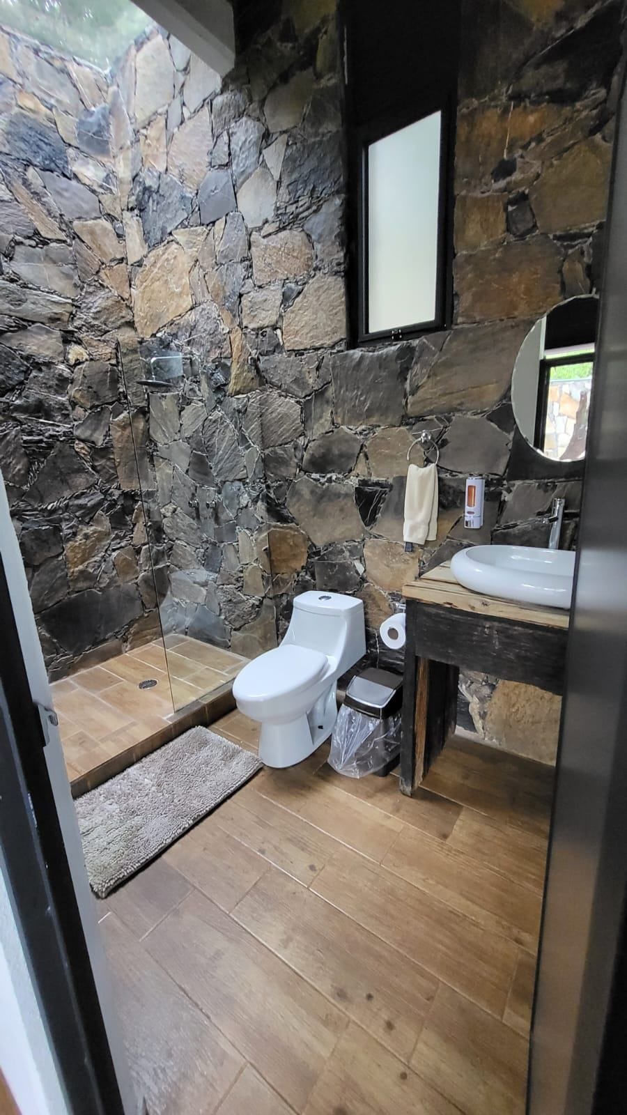 A bathroom with a stone wall, a toilet, a sink, and a mirror.