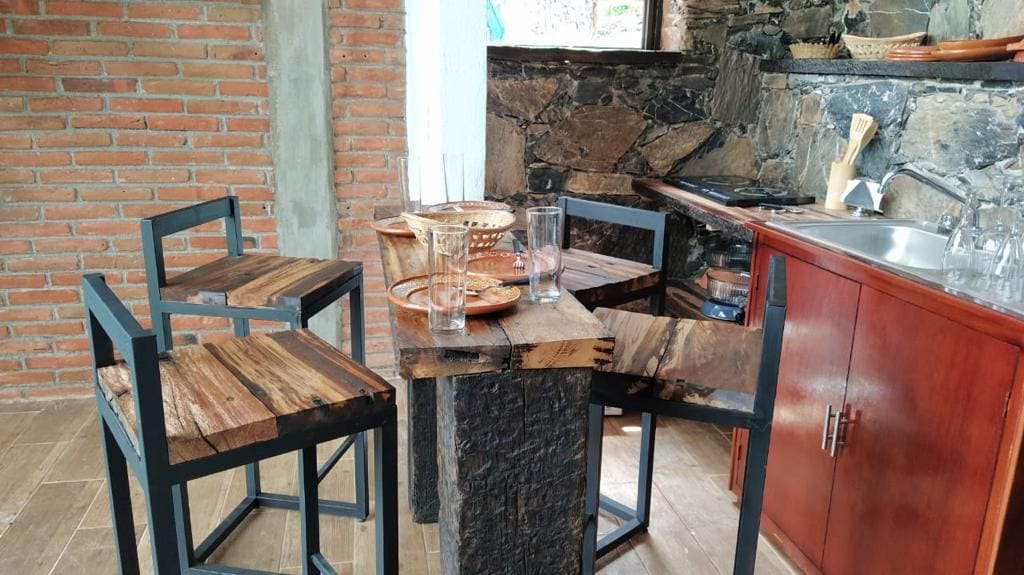 Une cuisine rustique avec un mur en briques, un plan de travail en pierre et des chaises en bois.