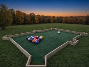A pool table with balls set up outdoors, surrounded by a wooden frame, with a grassy field and trees in the background. - View, Sauna, Free Spa, Dolly, and Anakeesta 155, (Gatlinburg)