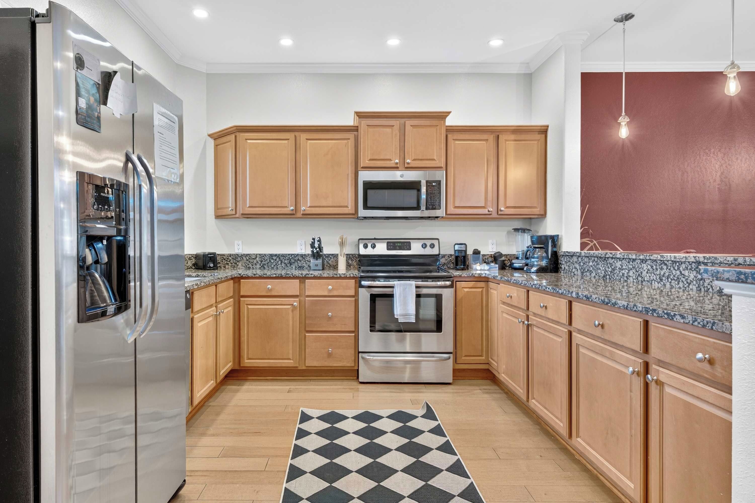 A kitchen with wooden cabinets, stainless steel appliances, granite countertops, and a checkered rug.
