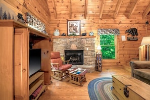 A log cabin interior with a stone fireplace, wooden furniture, and a television. - Hot Tub, Free Dollywood, Anakes, Sauna, Hot Spring (Gatlinburg)