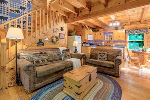 A cozy cabin interior with a staircase, two sofas, a wooden chest, and a kitchen area. - Hot Tub, Free Dollywood, Anakes, Sauna, Hot Spring (Gatlinburg)