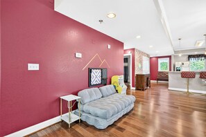 Una sala de estar moderna con una pared roja, un sofá gris, una mesita blanca y una máquina recreativa amarilla.