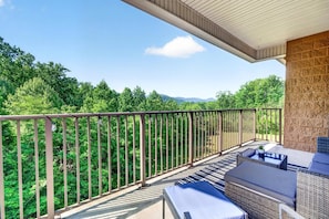 Ein Balkon mit Gartenmöbeln, einer Steinmauer und Blick auf eine bewaldete Landschaft.