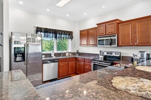 A modern kitchen with stainless steel appliances, wooden cabinets, granite countertops, and a window with a view of greenery. - Penthouse w/ Sauna, Arcade, Free Dollywood Tickets (Gatlinburg)