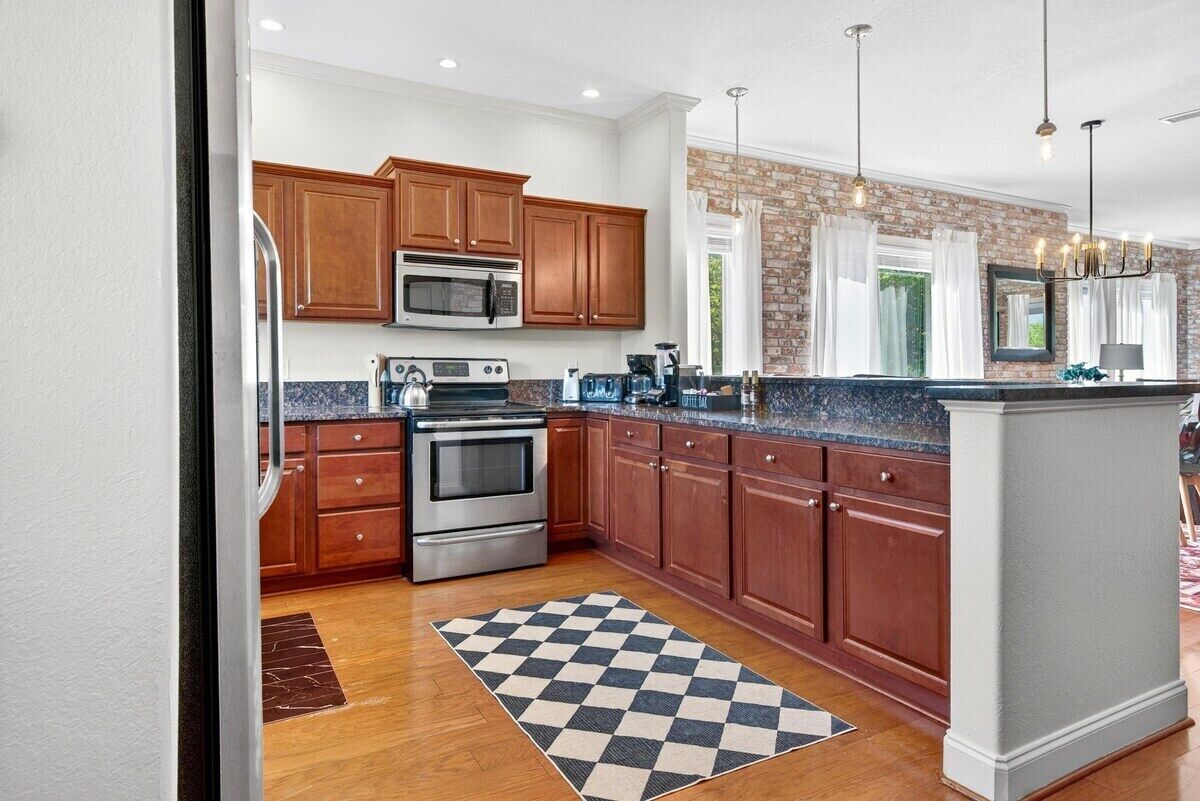 A kitchen with wooden cabinets, stainless steel appliances, and a checkered floor mat.