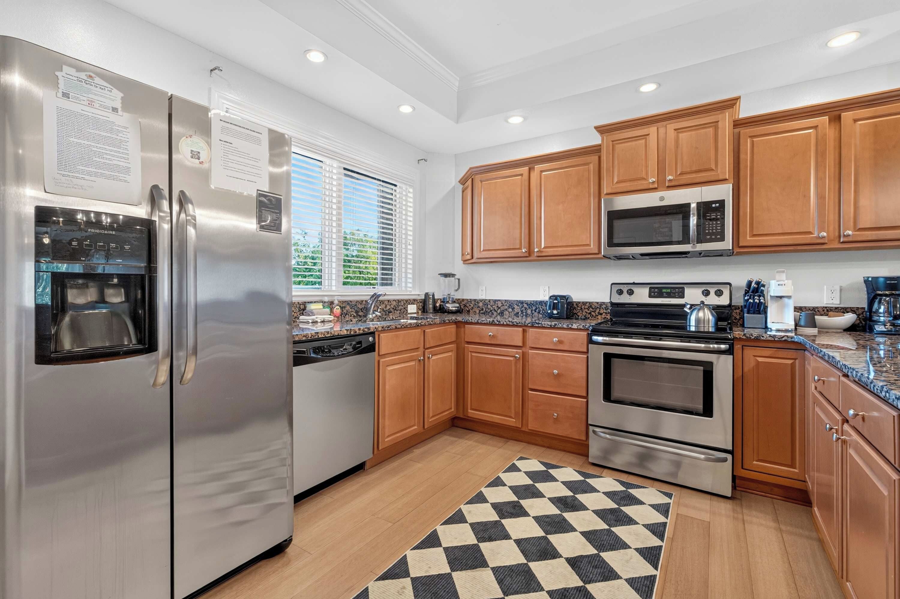 A modern kitchen with stainless steel appliances, wooden cabinets, and a checkered rug.