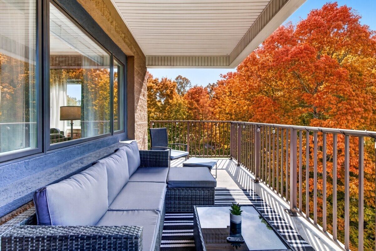 A balcony with a sofa and tables, overlooking a tree-lined view.