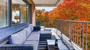 A balcony with a sofa and tables, overlooking a tree-lined view. - Gatlinburg Condo: Sauna, Arcade, Spa, Incredible (Gatlinburg)