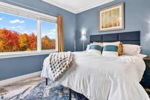A bedroom with a large bed, a window with a view of autumn trees, a framed picture on the wall, and a nightstand. - Gatlinburg Condo: Sauna, Arcade, Spa, Incredible (Gatlinburg)