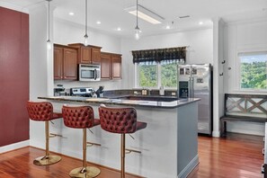 A kitchen with a central island, bar stools, wooden cabinets, a refrigerator, and a window with a view. - Luxury, Views, Free Tickets, Saunas, Arcade, Peace (Gatlinburg)