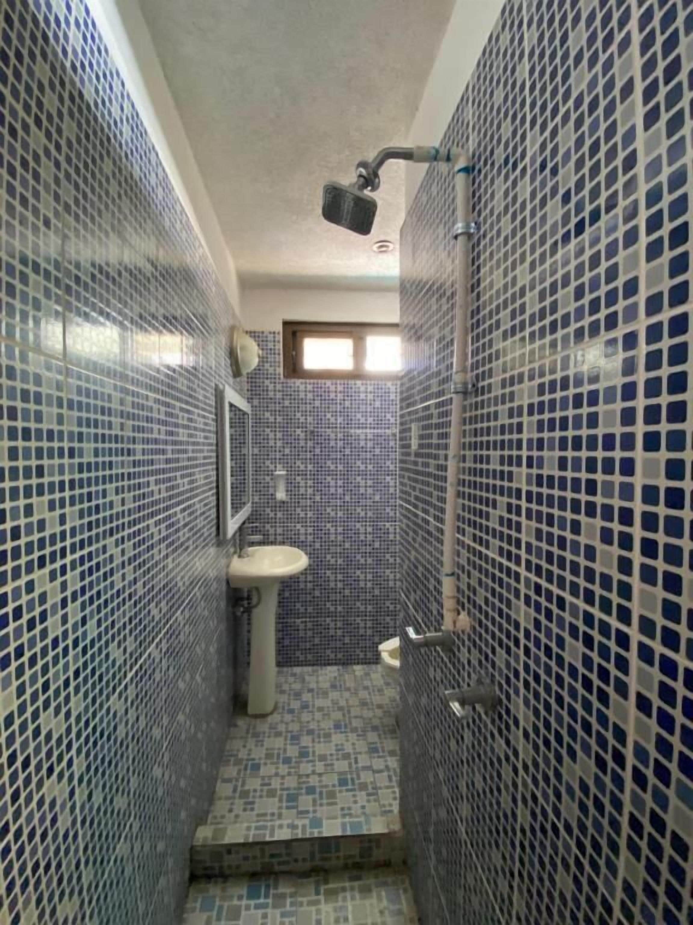 Ein schmales Badezimmer mit blauen Mosaikfliesen, einem Waschbecken und einer Dusche.