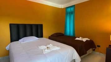 Habitación de hotel con cama, mesita de noche, ventana con cortinas y lámpara de pared.